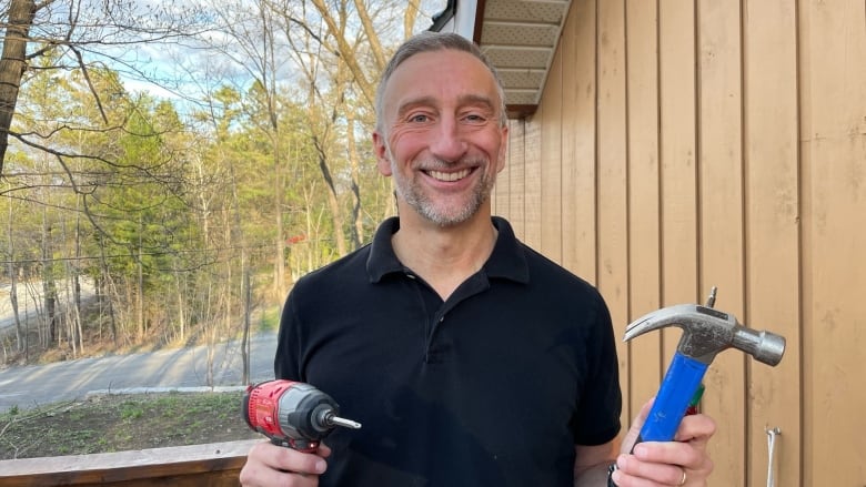 A smiling man holds power tools.