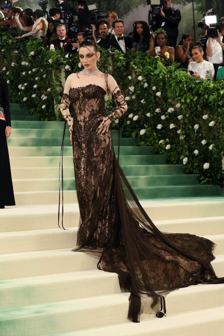 Emma Chamberlain on the Met Gala red carpet wearing a brown lacy corset dress with a long train. 