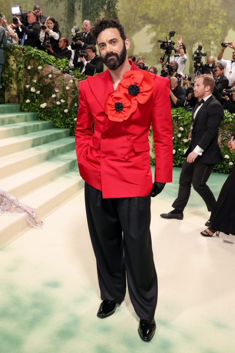 Morgan Spector on the Met Gala red carpet wearing a red and black double-breasted suit with oversized poppies on the lapel. 