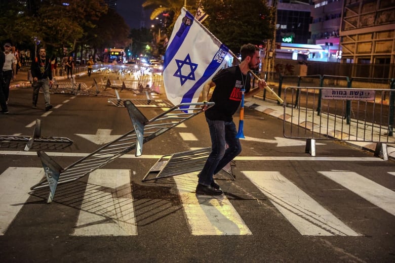 A protester carries an Israeli flag on a street.