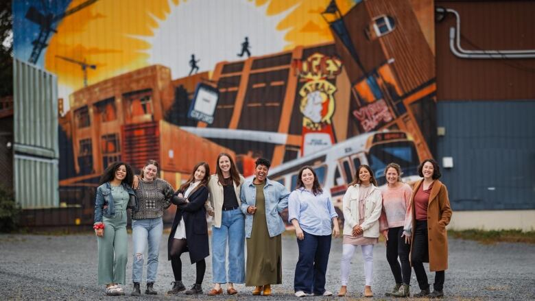 A group of people stand in front of a large mural and pose for a photo together.