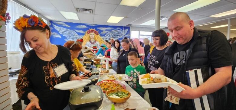 Lines of people on both sides of a table picking up the food on the table. 