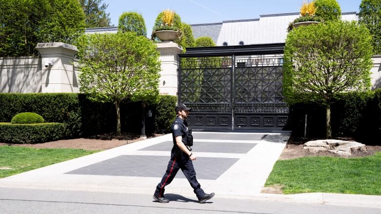 A police officer walks outside a gated mansion. 