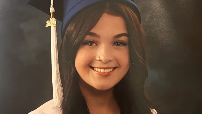 Woman wears graduation cap and gown and smiles at camera