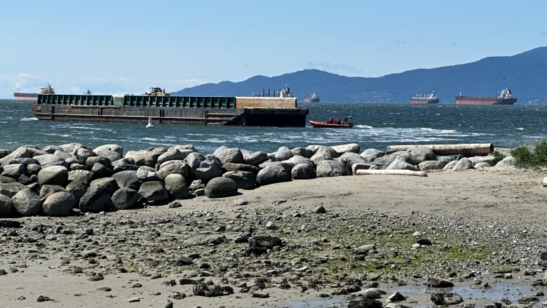 A large barge is seen on a picturesque sunny day being towed by smaller vessels.