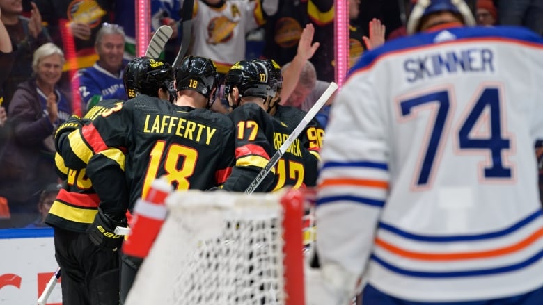 Hockey players celebrate after a goal with opposing goalie in foreground