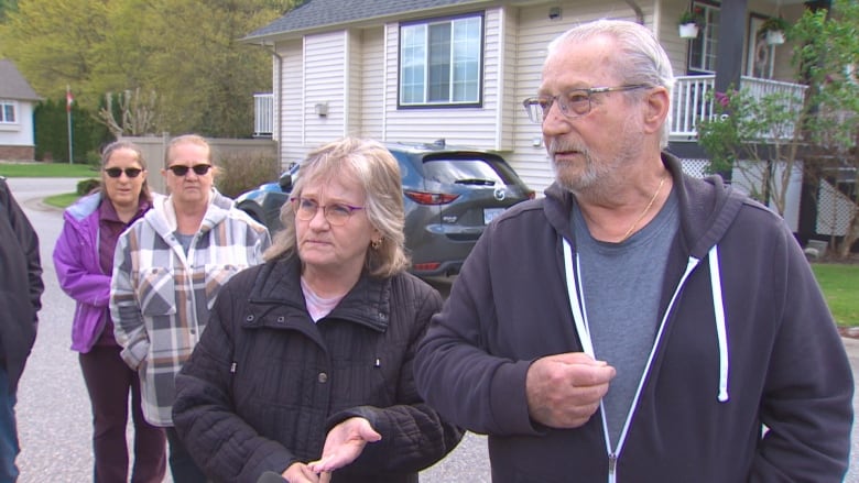 A retired couple stand together outside in a residential area.