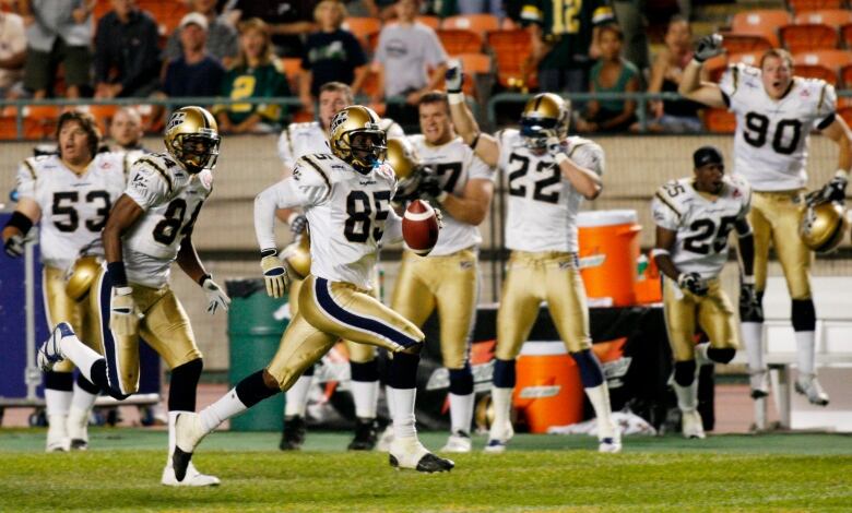 A player runs with the football, while his teammates on the sideline jump and cheer.