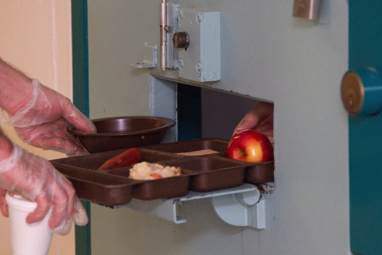 A food tray is passed through a small opening in a steel door.