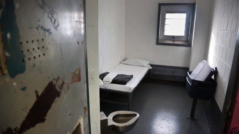 A small jail cell with a single window and steel door.