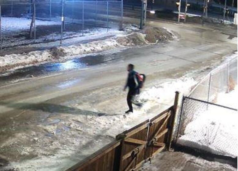 A person walks at night on a snowy street. The image is blurry and the person is seen from above.