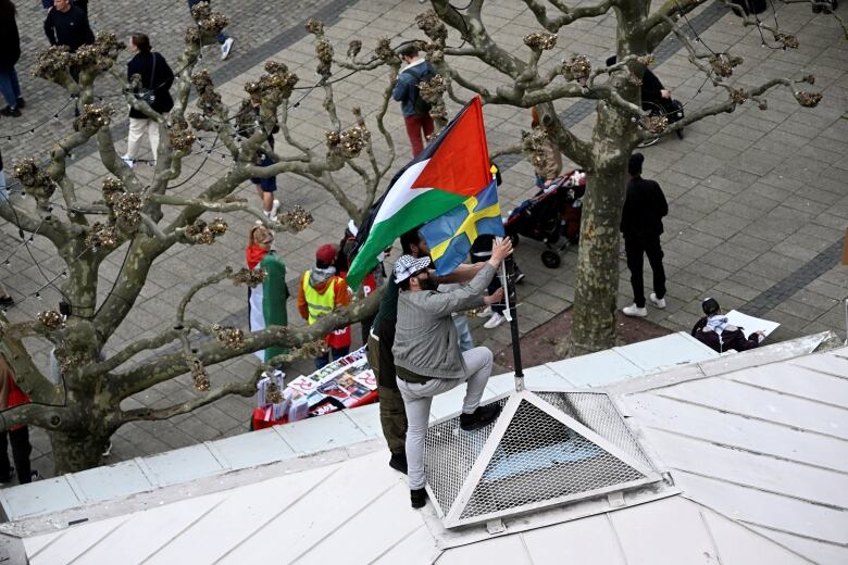 A man puts a Palestinian flag and a Swedish flag on a rooftop. 