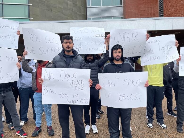 Two men holding signs stand in front of a group of other protesters.