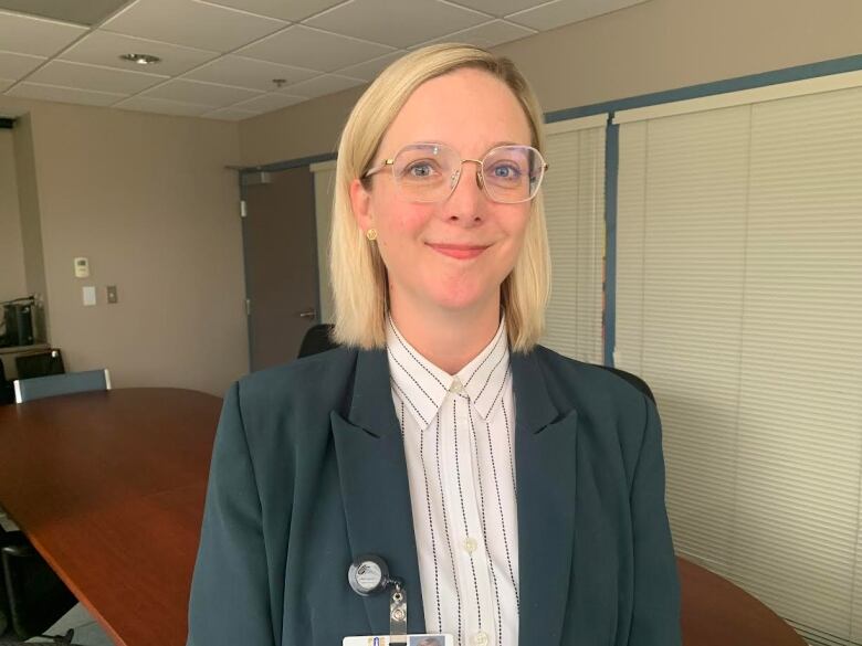 A smiling woman with blonde hair and glasses stands in a board room.