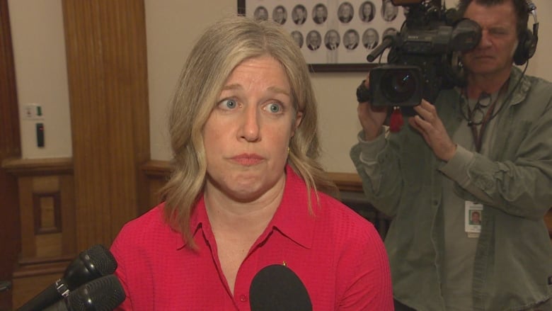 A blond woman in a red dress is unsmiling in front of reporters.