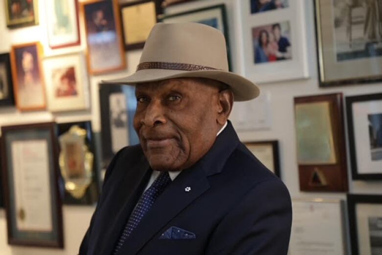 Man wearing a hat standing in front of a wall of photos.