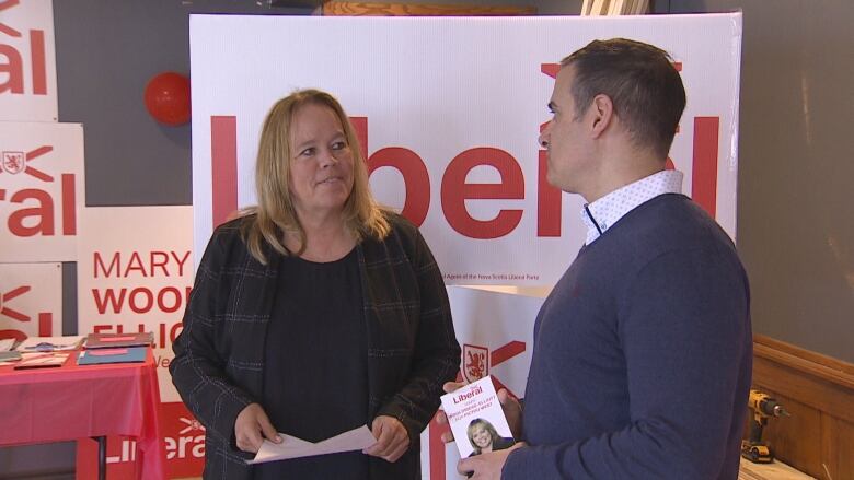 tow liberal representatives speak in front of political signage 