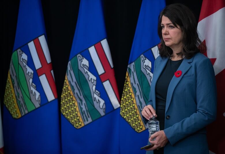 A woman stands by flags, drinking water.