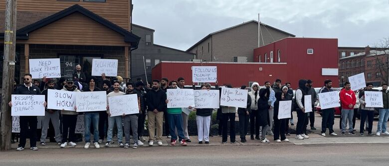 People holding signs stand in front of buildings.