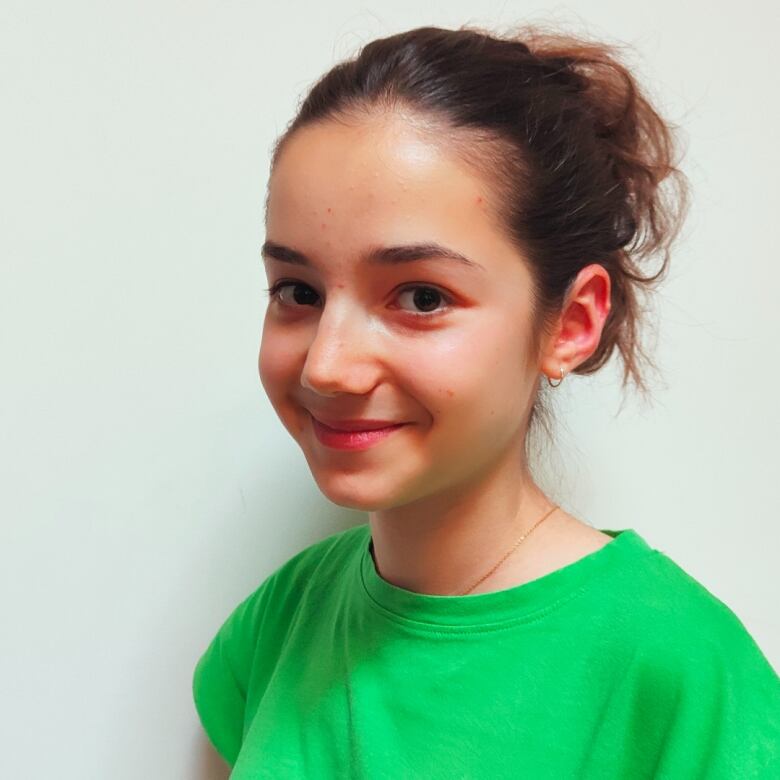 A teenage girl with brown hair who is wearing a green T-shirt smiles at the camera.