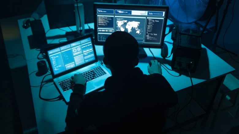 A man looks at blue-tinted screens with a large fan next to him.