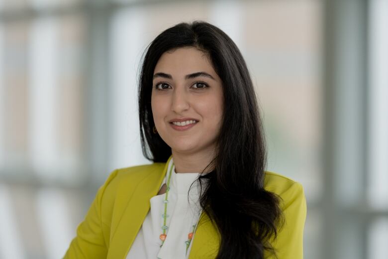 A woman with long black hair is seen wearing a chartreuse jacket with a white blouse.