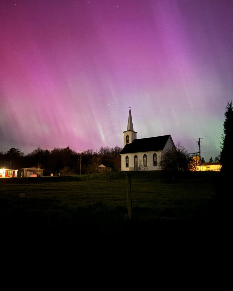 A church is seen in the foreground with northern lights illuminating the sky behind.