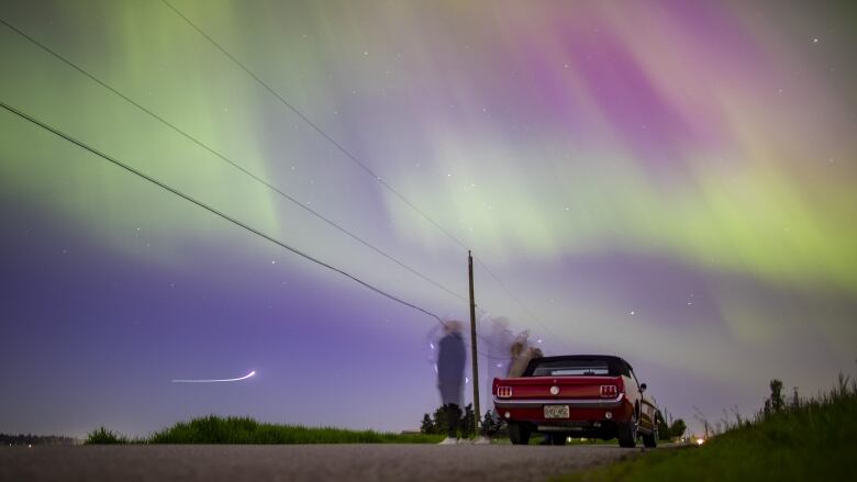 People lean against a designer car as they take pictures of the northern lights.