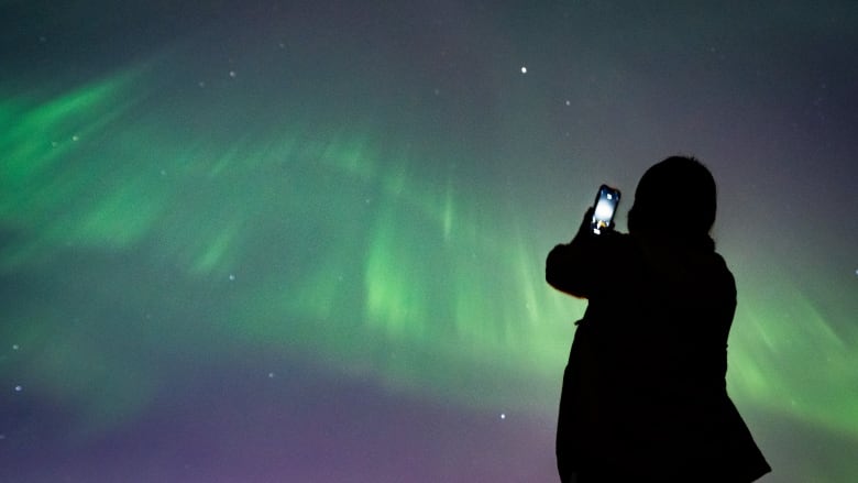 A person takes a picture of northern lights above them.