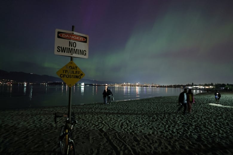 People are pictured at a beach with the northern lights above them.