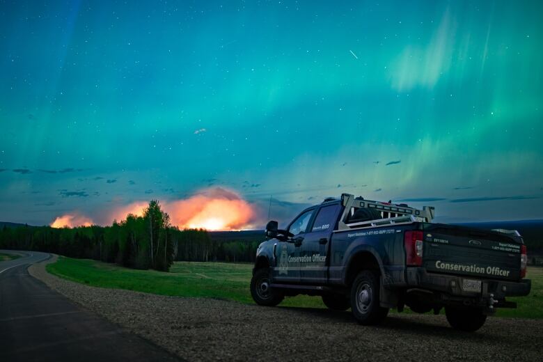 Plumes of smoke arise from a fire with the northern lights just above it.