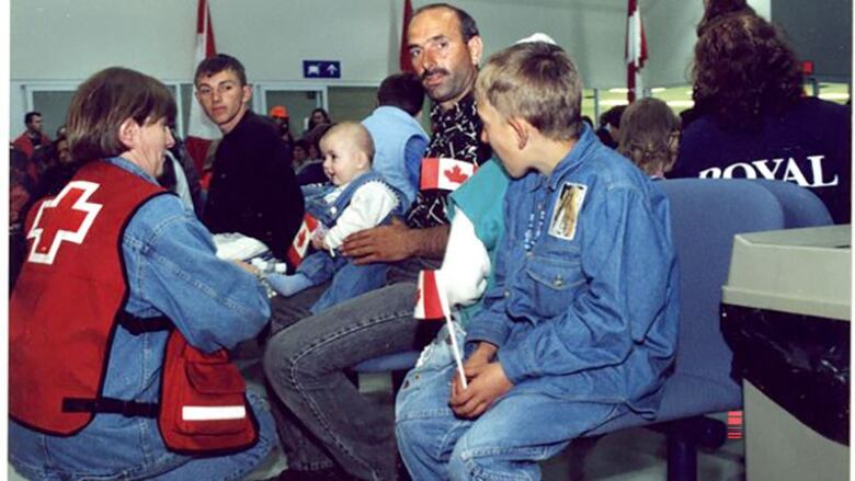 A red cross official attends to a family holding small Canadian flags.