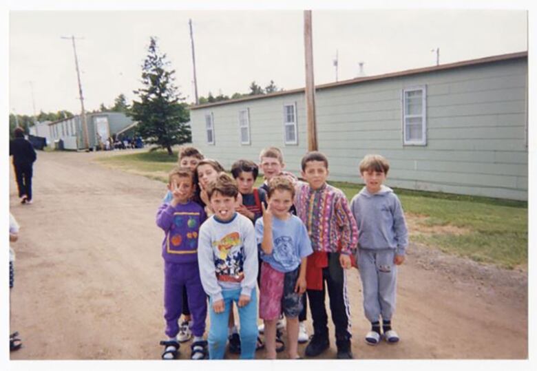 A group of small children stand on a dirt road in a housing settlement.