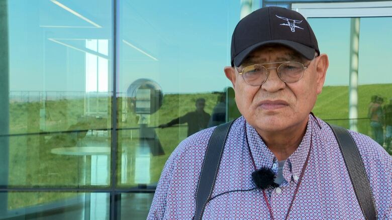 A man wears glasses and a baseball cap and looks at the camera. 