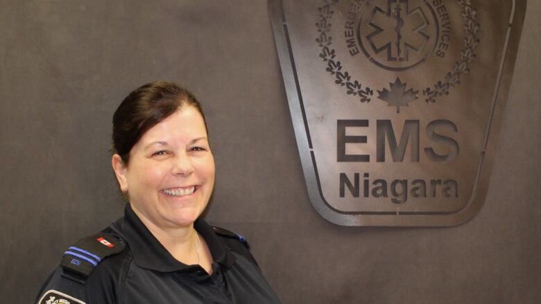 A woman in uniform stands in front of a Niagara EMS sign. 