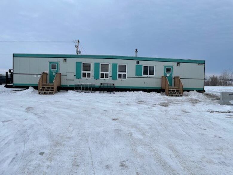 Photo of white and green trailer on a plot of land in the snow.