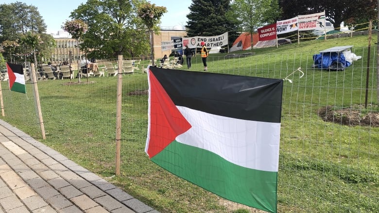 Palestine flag hung on makeshift fence, demonstrators are visible in the background