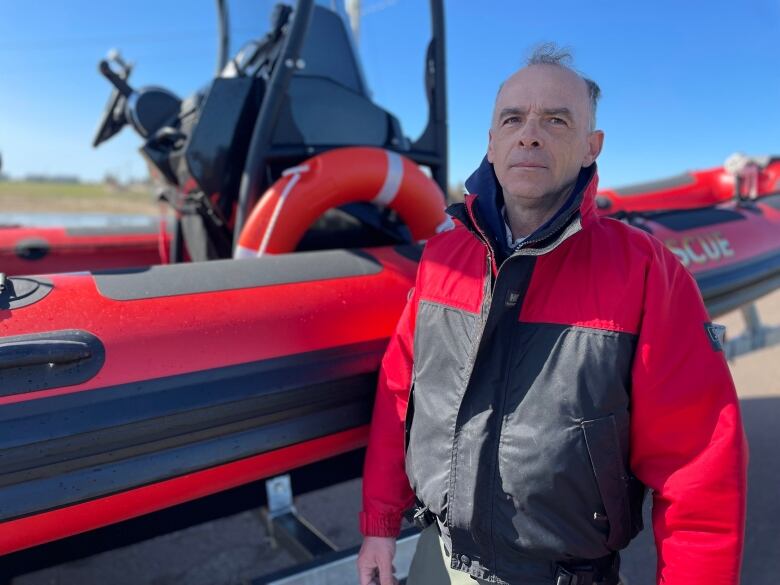 A firefighter in a red and black jacket stands in front of a red Zodiac boat. 