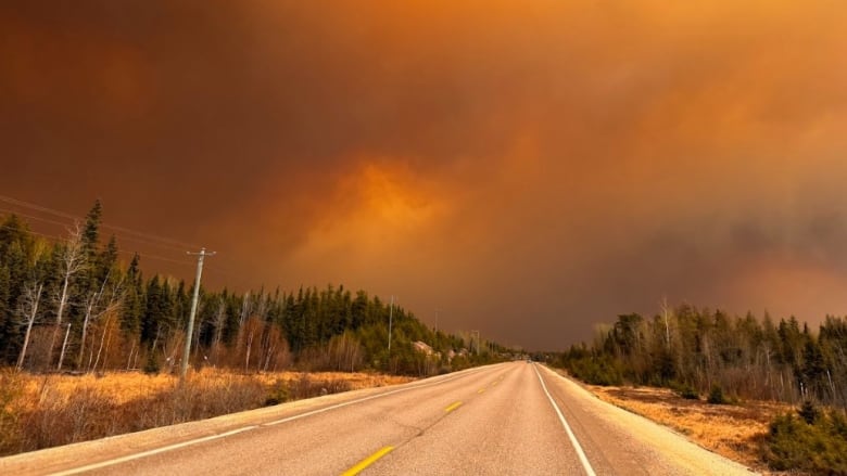 The sky above a highway is black and grey and orange with smoke from forest fires. 