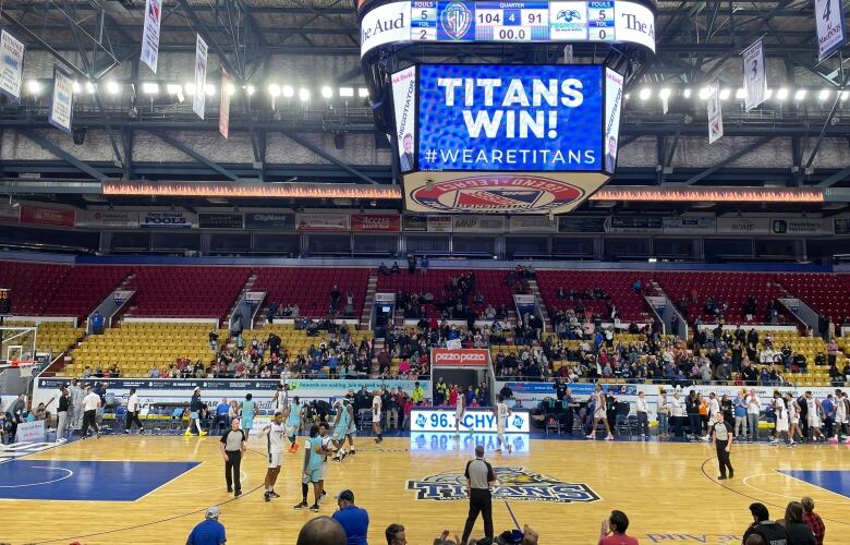 Basketball players on a court with the screen above them reading 