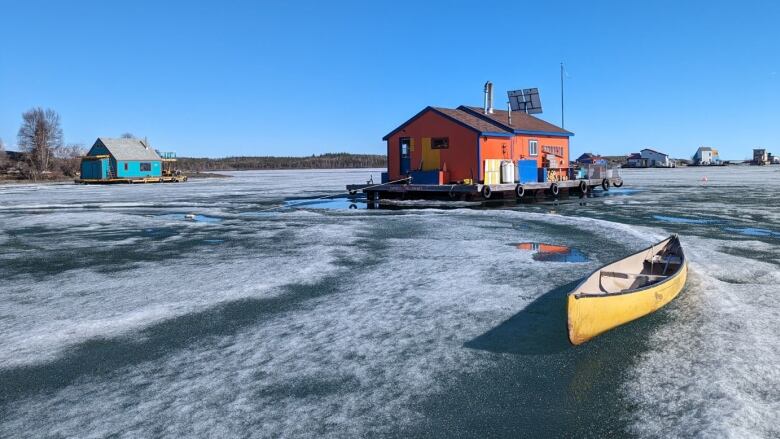 A canoe and some houseboats sit on some icy ground.