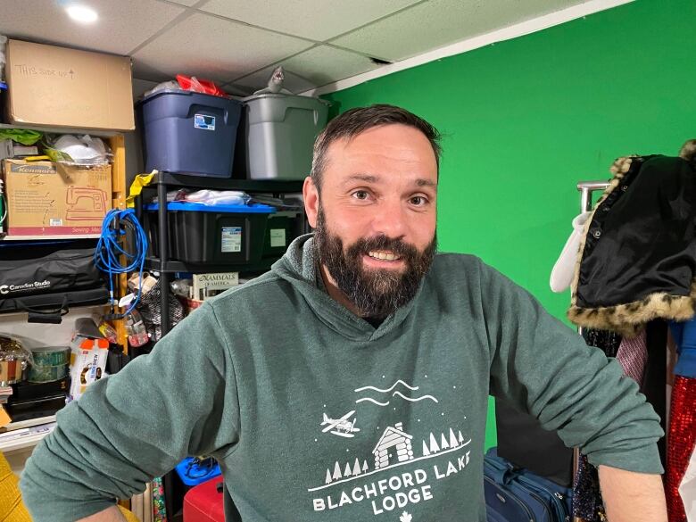 A bearded man sits in a room with storage bins and shelves.