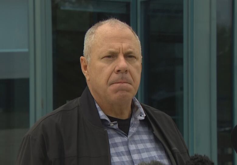 A man stands outside a building in front of microphones.