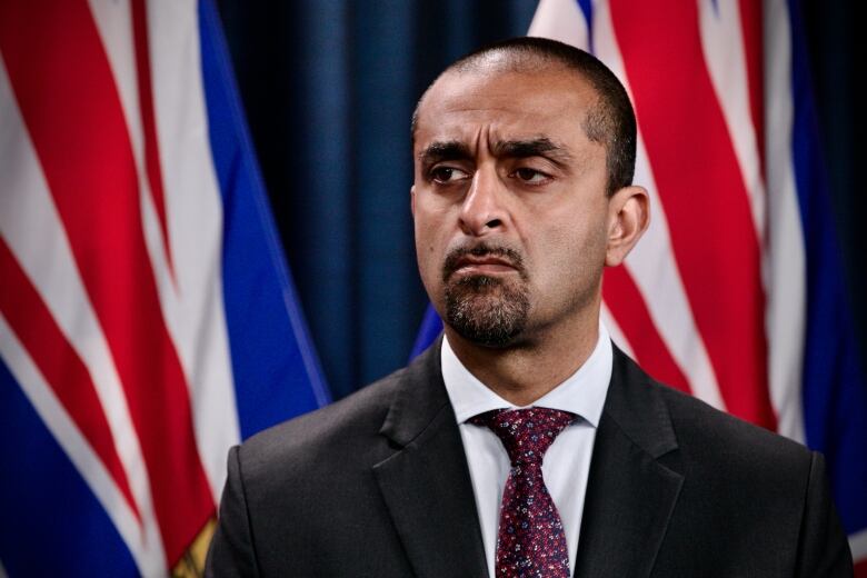 A South Asian man looks to the side, while in front of B.C. flags.