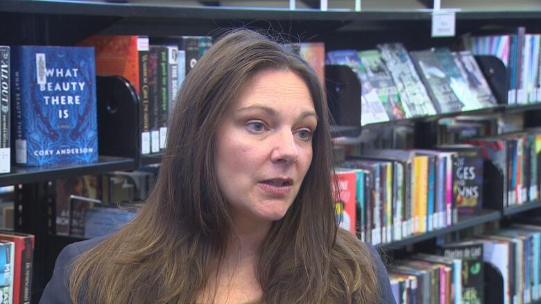 A woman speaks with library bookshelves behind her.