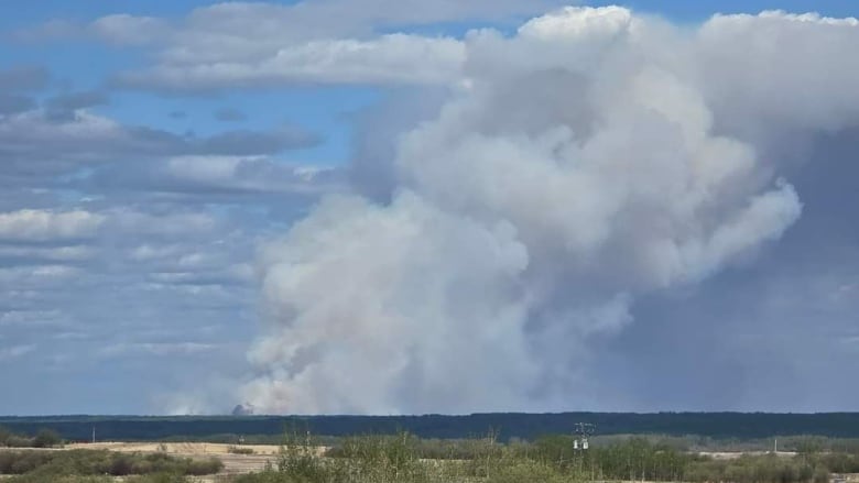 Plumes of smoke rise from a fire on a partly cloudy day.