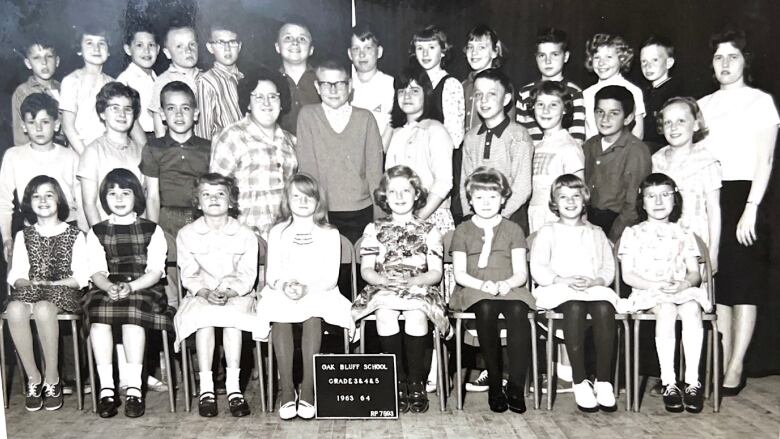 Marlene Mutch stands with her class of 1963 for a school photo at Oaf Bluff School. Children in the front row sits on chairs and the back two rows stand. 