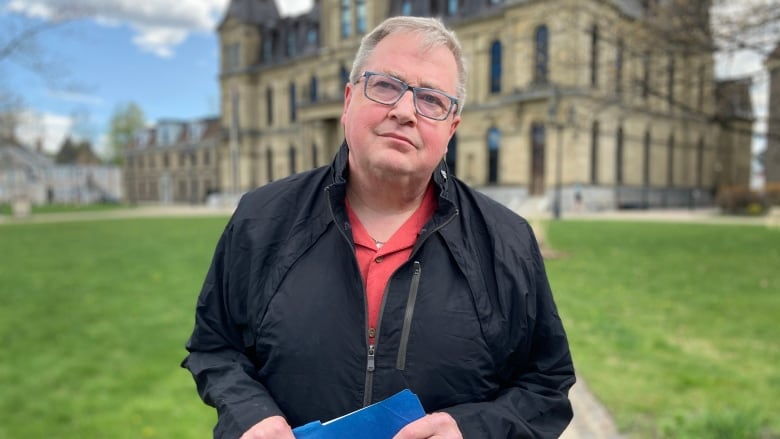 A man wearing a black jacket and holding a blue file folder