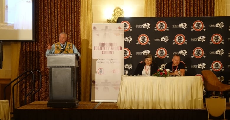 One person speaks at a podium with two others seated beside him.