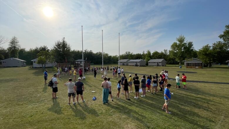 Children gather on a sports field in the summer.